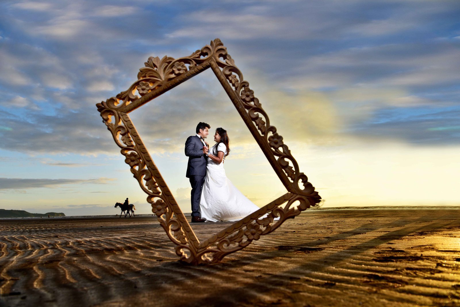 Wedding couple inside a large golden picture frame on the beach