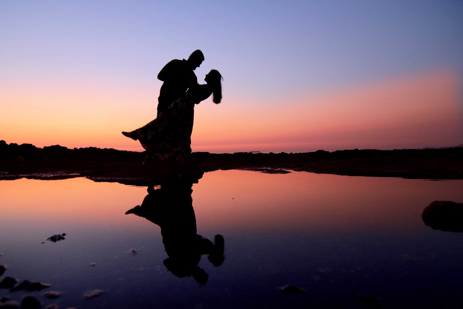 Couple silhouetted above still water at sunset
