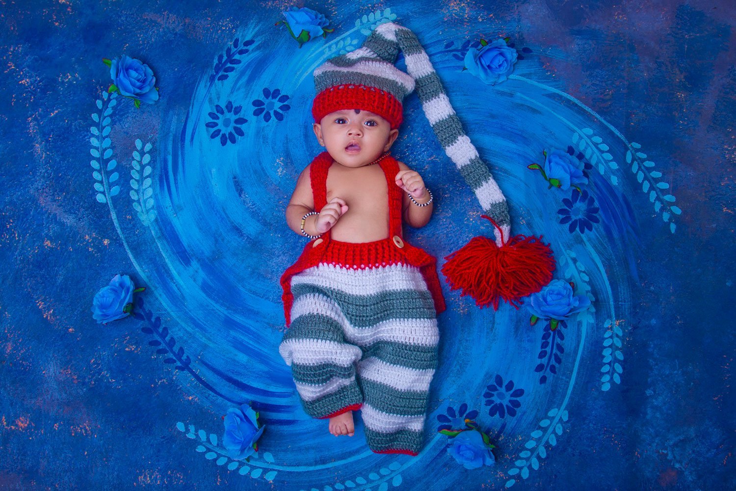 Baby wearing a red hat nestled in a blue knitted blanket